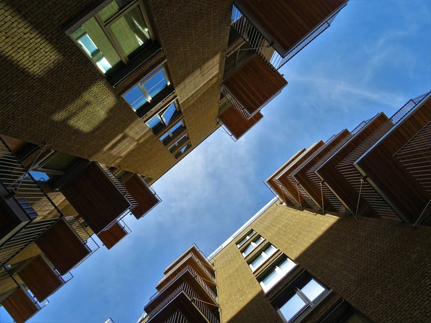 A modern multi-storey residential building with numerous glass-paneled balconies arranged on each floor. The building features a combination of smooth and textured exterior surfaces, with large window