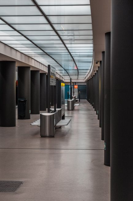 A modern, clean interior of an office or public space near Uxbridge Station, featuring smooth wooden flooring and tall, cylindrical black columns arranged in parallel lines. The ceiling has a curved, 